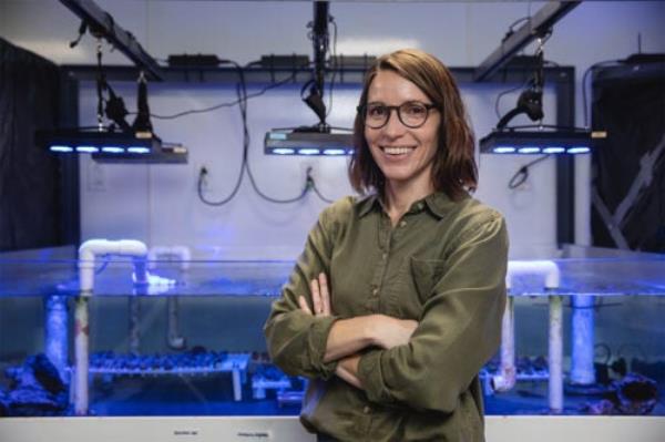 A smiling person poses in front of an aquarium.