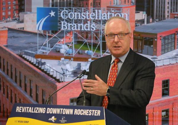 Bill Newlands, President and CEO of Constellation Brands, speaking at a podium during the grand opening of their new headquarters in downtown Rochester.